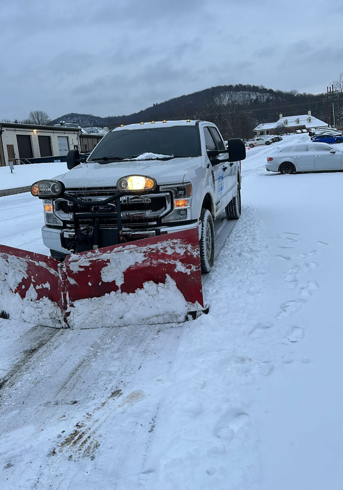 Pickup truck with a red V-plow clearing snow from a commercial parking lot in New Jersey