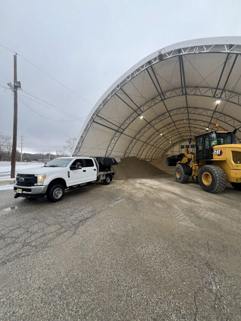 JRW Services truck and wheel loader at a hoop-style salt barn stocked for winter